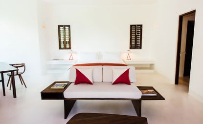 Bedroom of the Hotel Esencia in Mexico with a white bed, wooden furniture and shutters at the windows