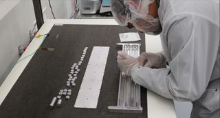 a scientist in a clean suit bends over a table containing small metal disks