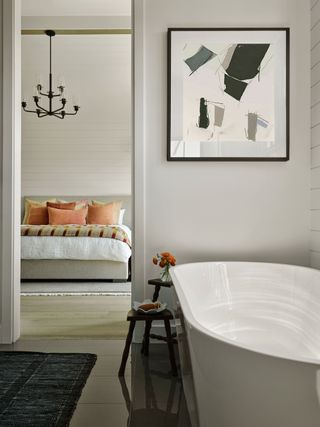 primary ensuite with freestanding bathtub and modern artwork on white walls
