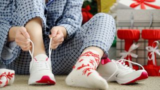 Woman lacing up running shoes beside pile of Christmas gifts