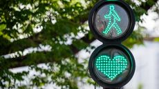 A traffic light shows green for pedestrians and also a heart in green lights.