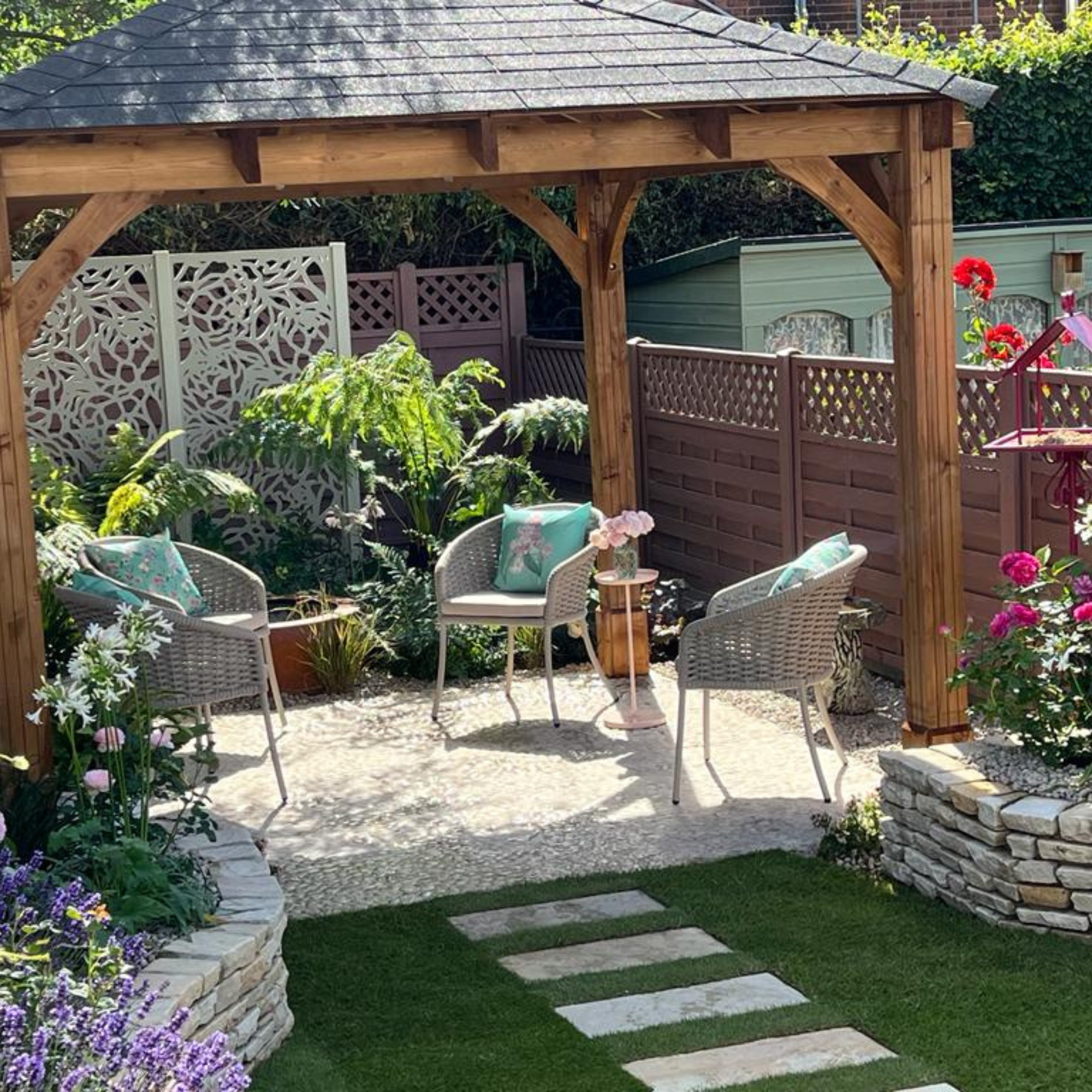 Purple painted garden fence, pergola and seating area with three garden chairs.