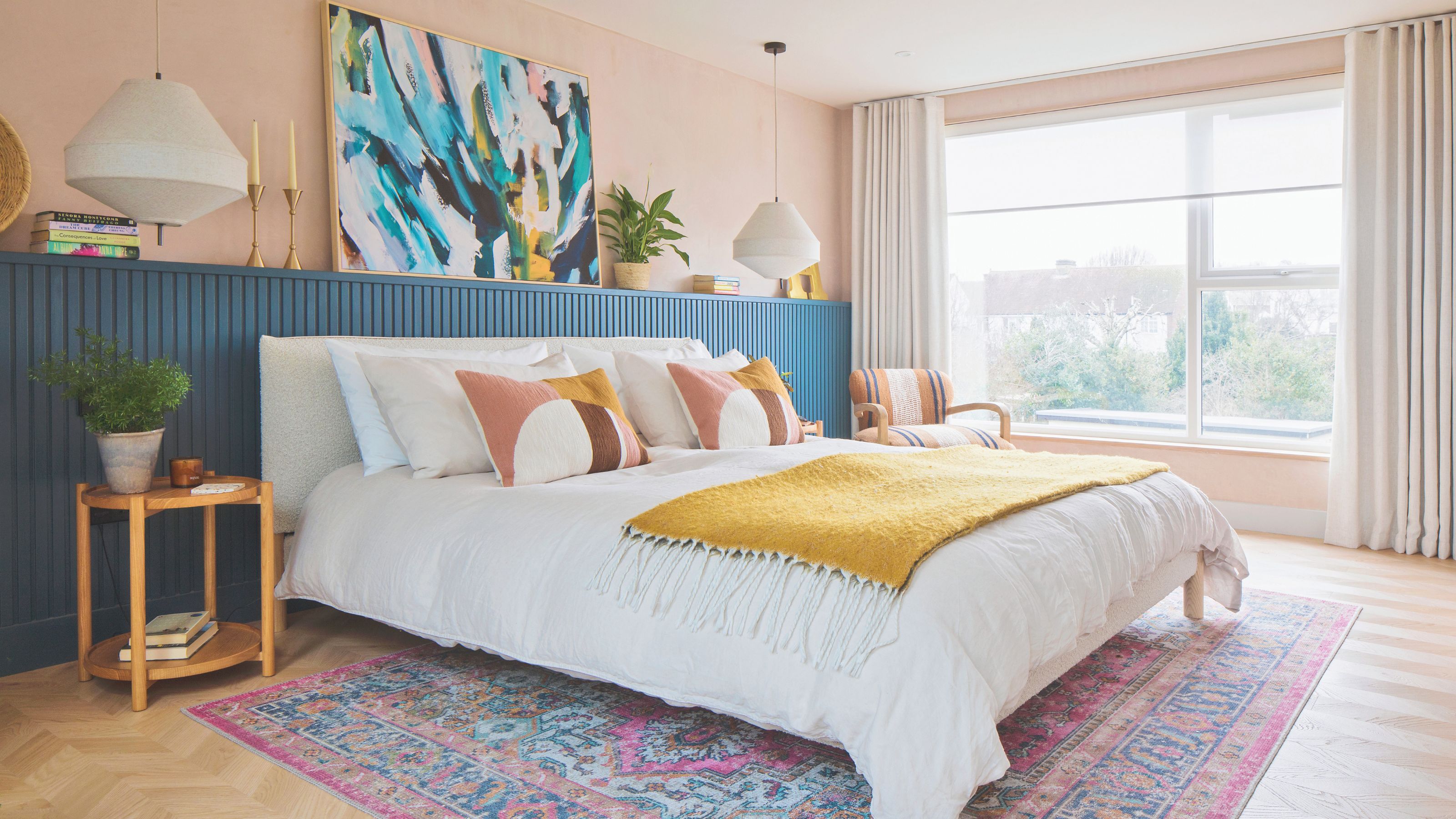 Colourful master bedroom with large bed, wall panelling, colourful artwork and multicoloured rug beneath the bed