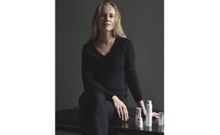 NUORI founder Jasmi Bonnen photographer in all black, next to her line of skincare products.