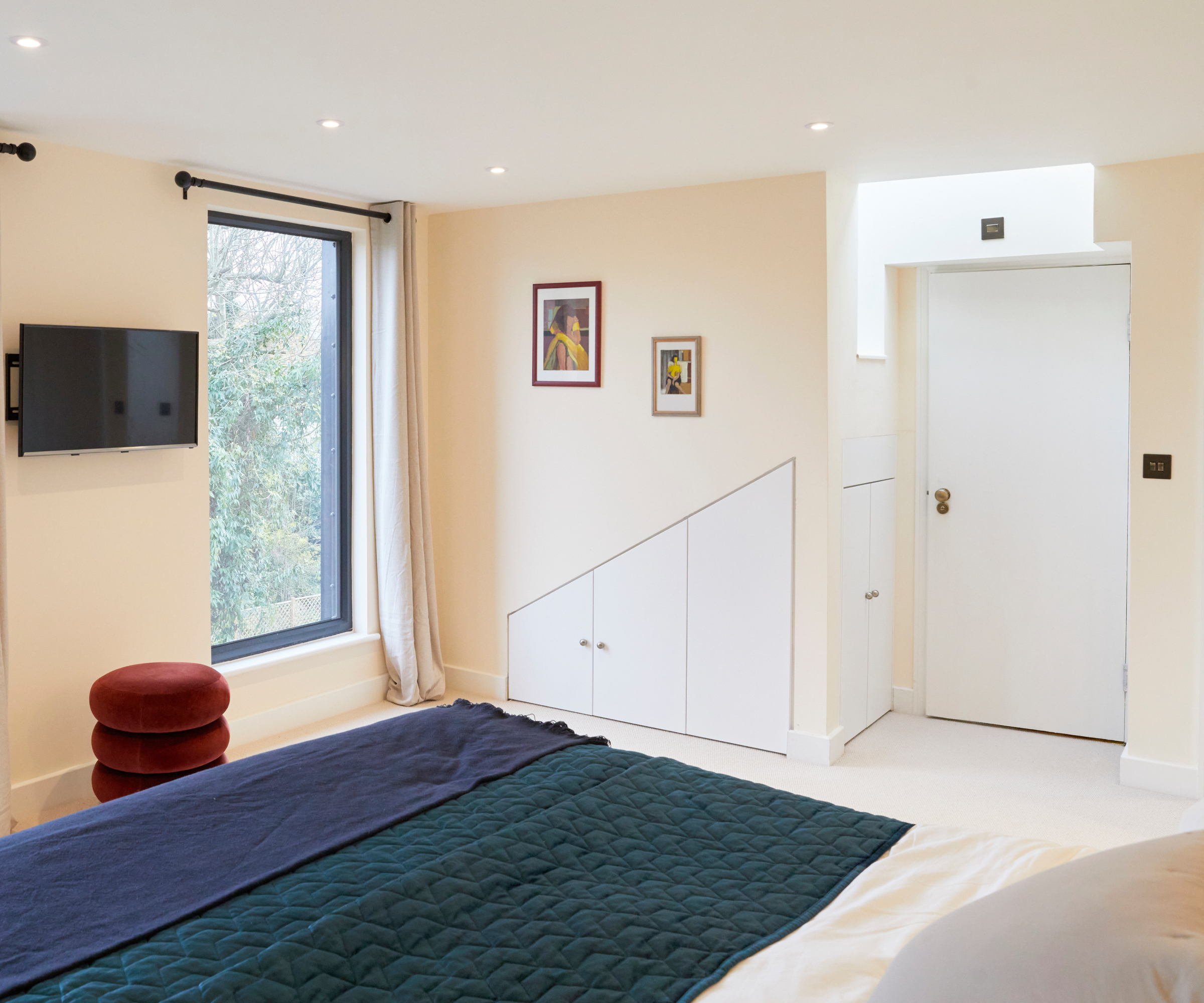 bedroom of dormer loft conversion with built in storage in wall, door leading to bathroom, large picture windows, cream walls and light carpet