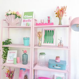 Pink shelving dressed with bright accessories, frames, and plants