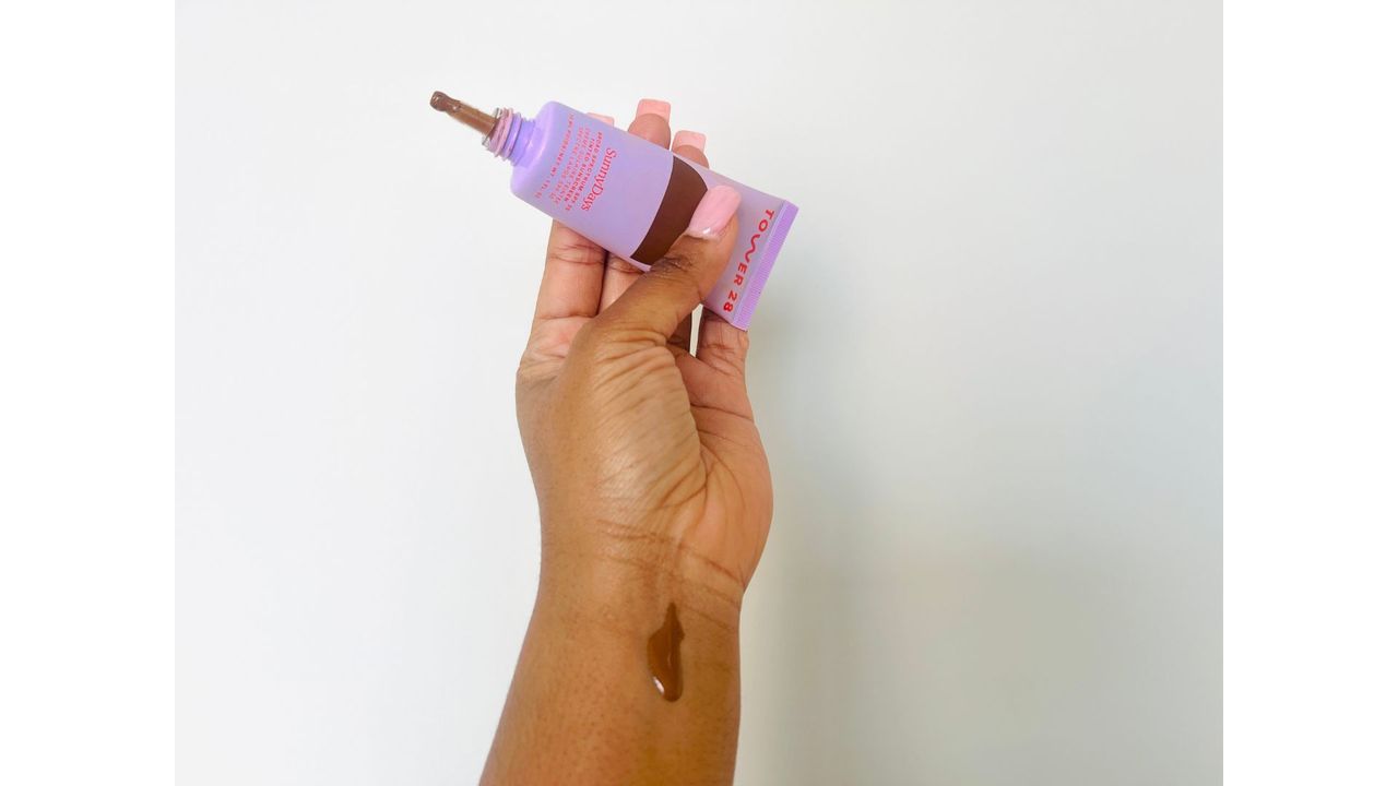 A person holding an open purple squeeze tube of one of the best tinted moisturizers with SPF.