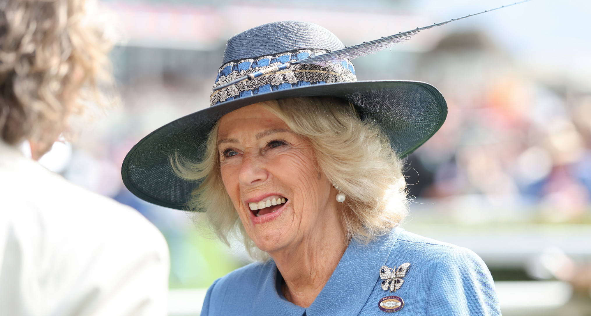 Queen Camilla smiling, wearing a blue hat and coat