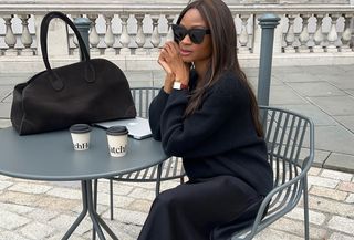 Woman wearing a black sweater, black trousers, and black sunglasses.