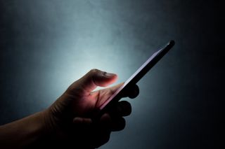 An anonymous mobile phone user using their device in a darkened room