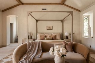 A bedroom with textural walls, a four poster bed and a curving sofa