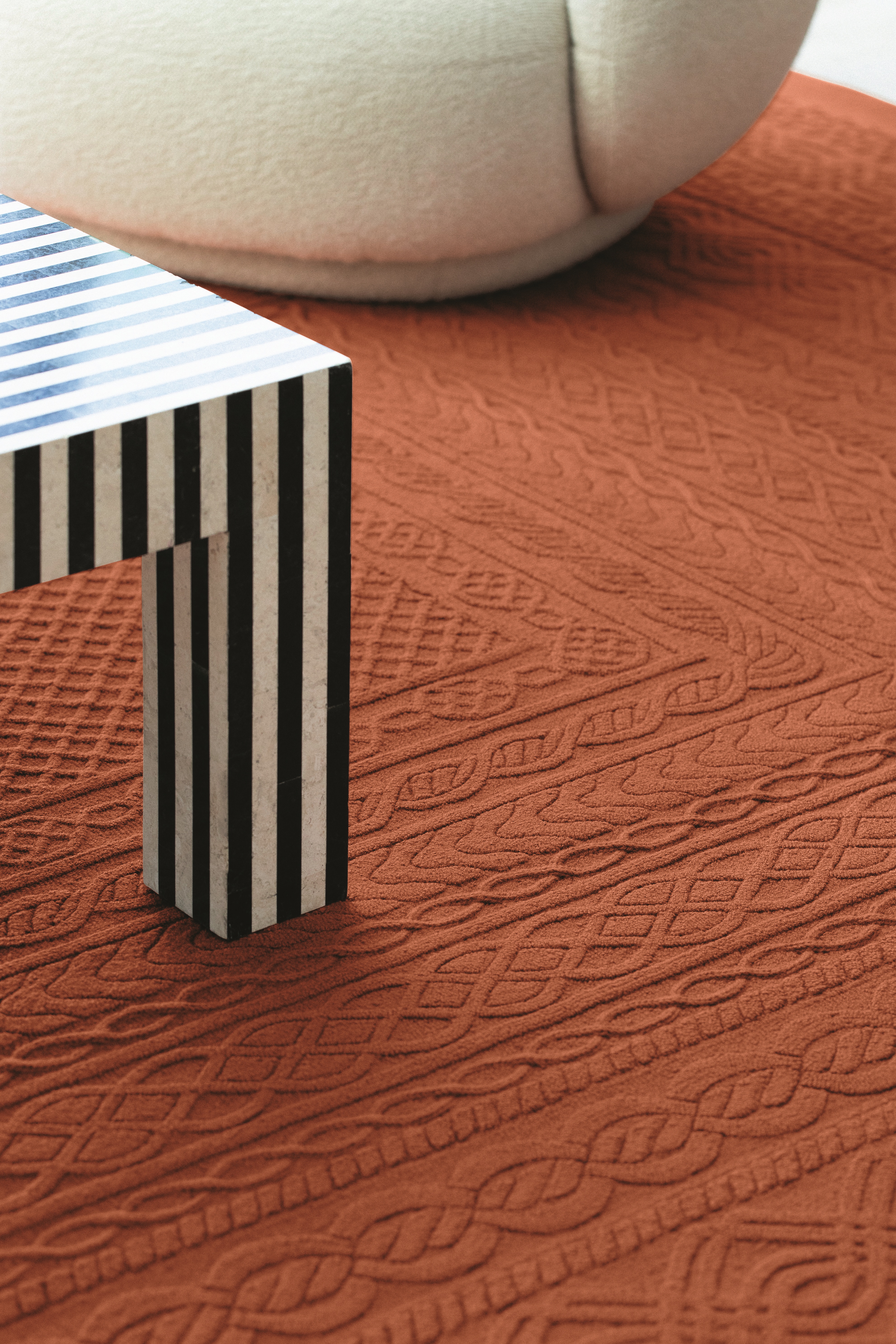 A terracotta-hued, textural rug boasts knots-looking patterns as it lays under a striped coffee table and a chubby shearling armchair in white.