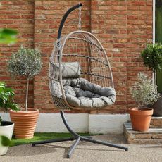 Cocoon chair hanging on steel frame in garden in front of red brick wall