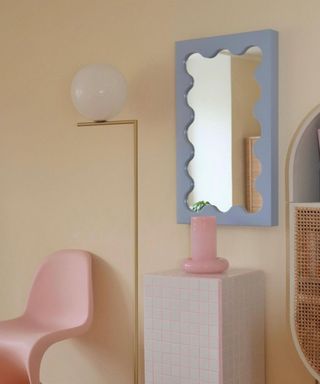 blue ripple mirror in room with pink chair, gold lamp and white tiled side table
