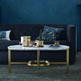 White marble coffee table with brass detailing with drinks in front of a blue couch