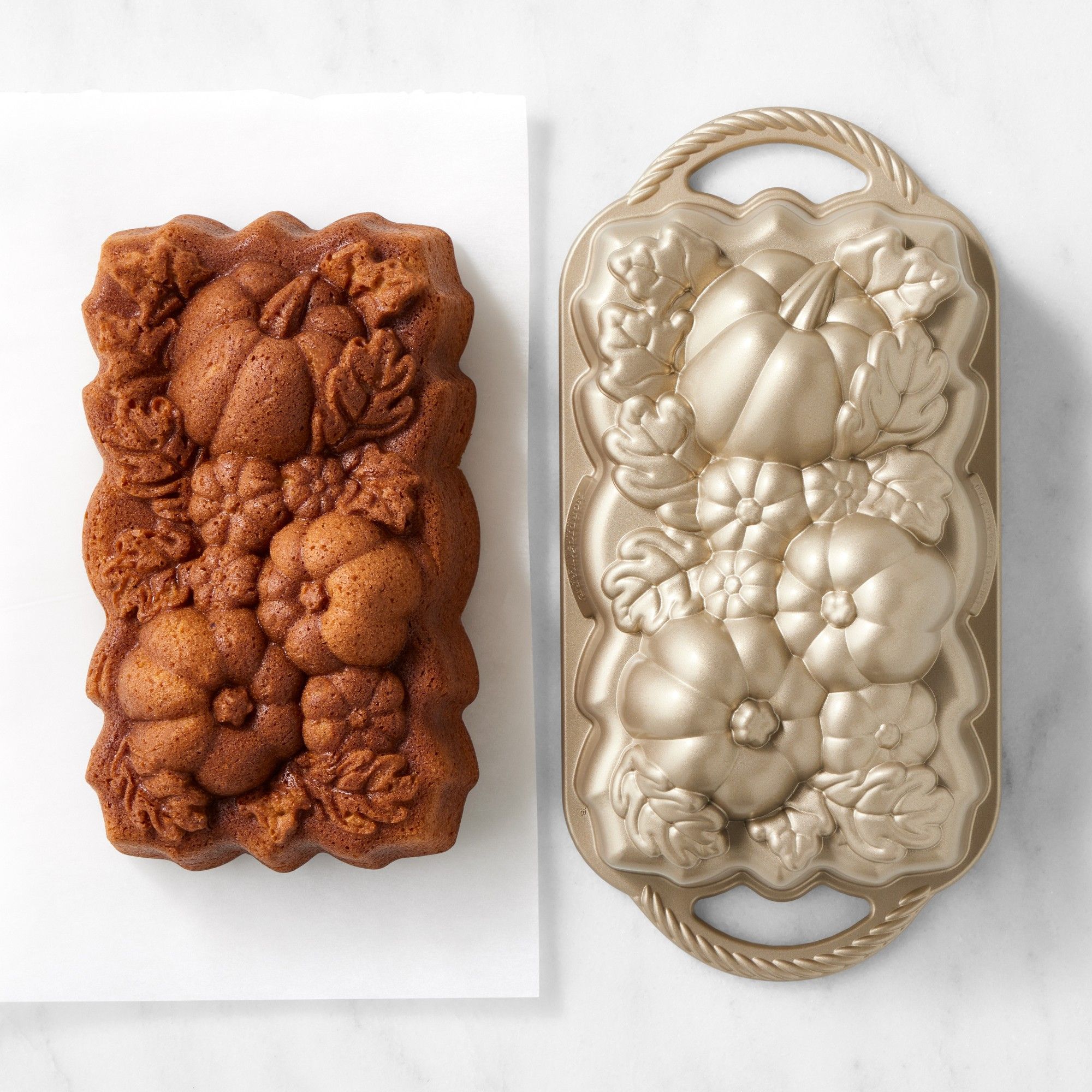 A baking tin with pumpkins carved into the top, beside a loaf cake.