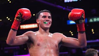 Boxer David Benavidez, wearing a mouthguard striped with the colours of the Mexican flag, raises his gloves ahead of the Benavidez vs Andrade fight.