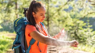 A woman applies mosquito spray to her hands during hiking