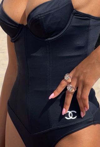 a close photo of a woman wearing the black-and-white swimsuit trend in the form of a black one-piece with white Chanel logo