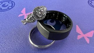 The Oura gen 3 smart ring with other silver jewellery against a purple background.