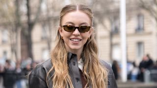 Sydney Sweeney on the streets of Paris in Miu Miu ensemble with brown Beau bag, shades and a black miniskirt and jacket. Oh, and leg warmers.