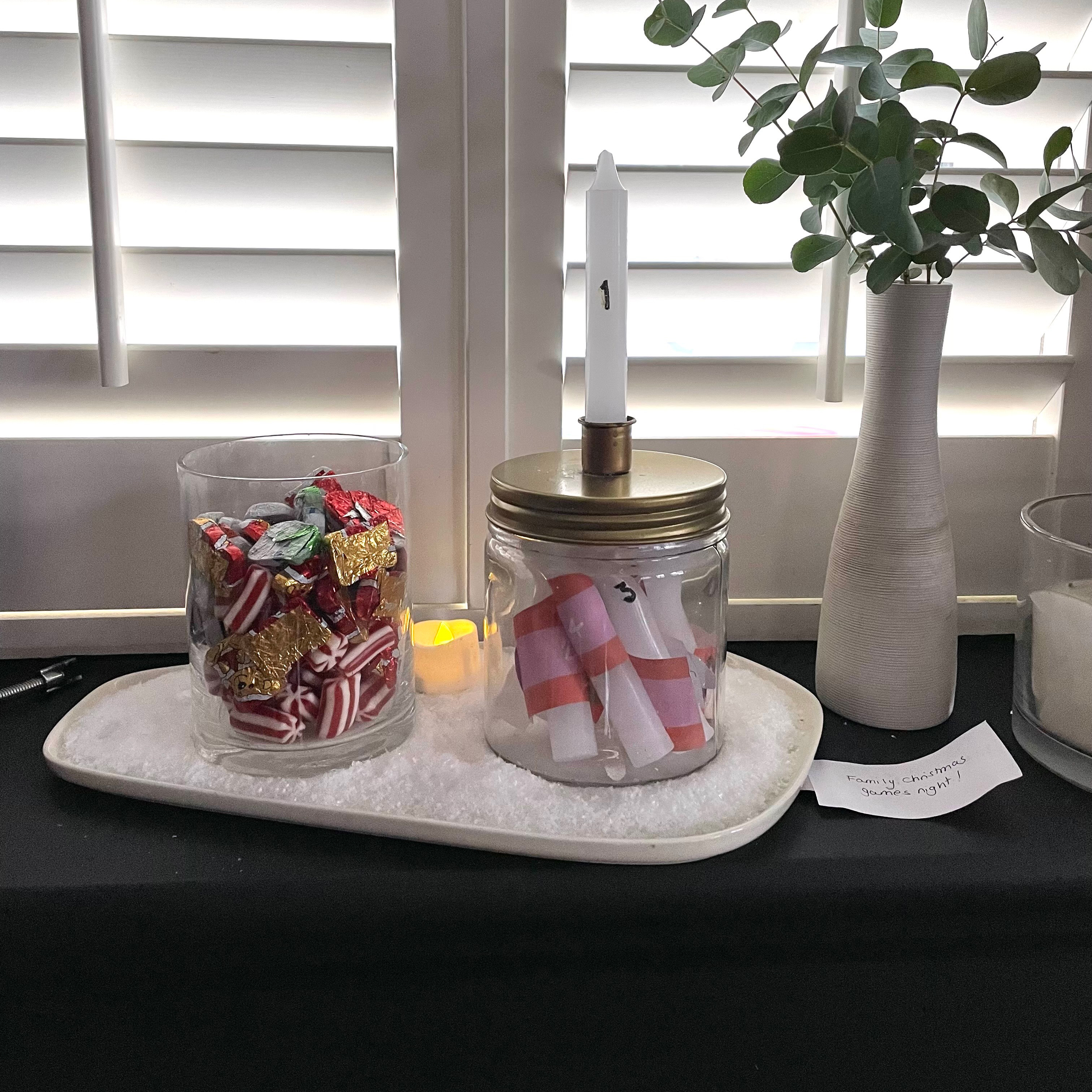 White ceramic tray with two jars on it, one full of foil-wrapped festive chocolates and the other filled with candles