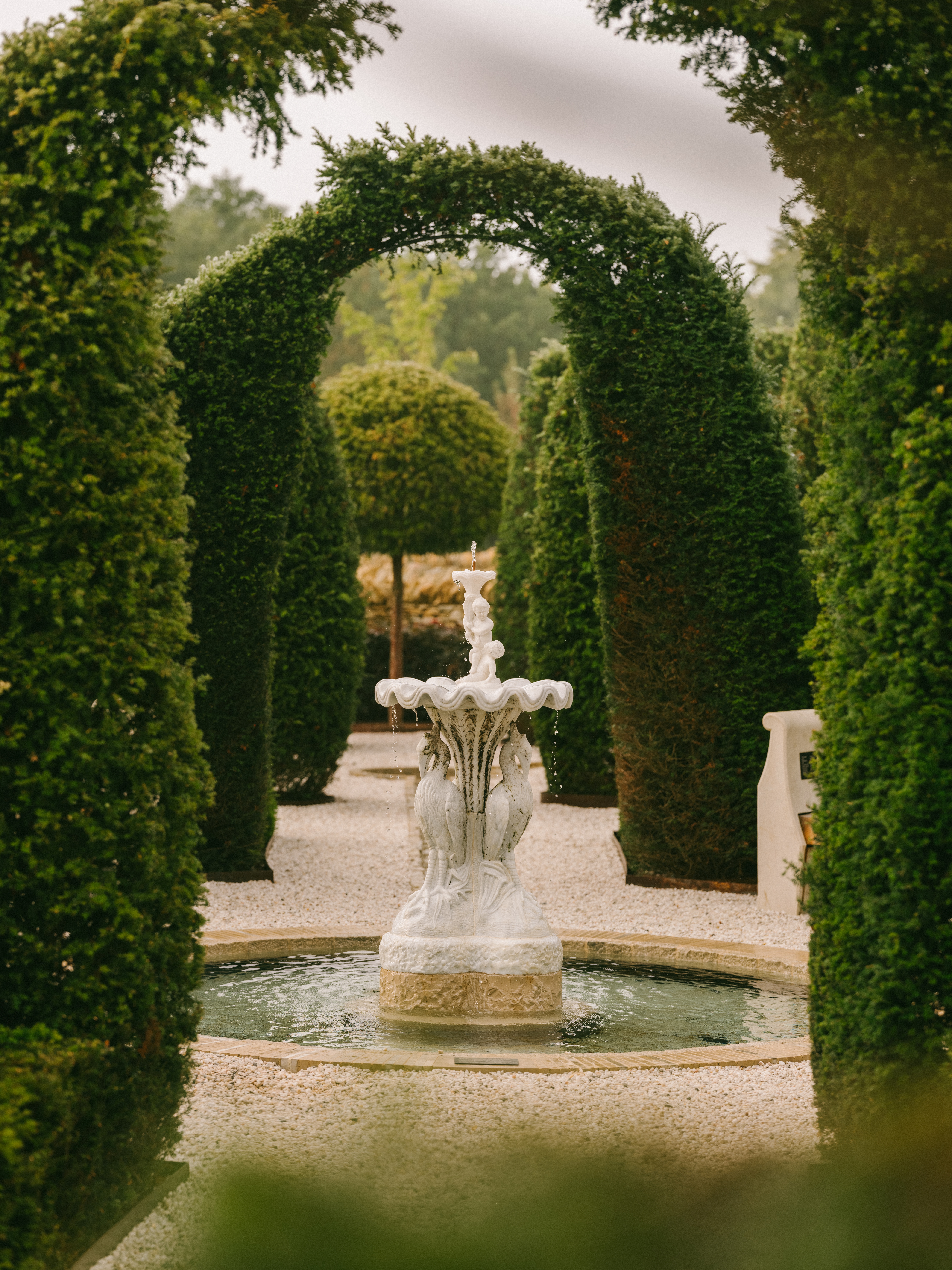 A bucolic garden with a central water play, complete with a rock sculpture inspired by marine life, and arched hedges.