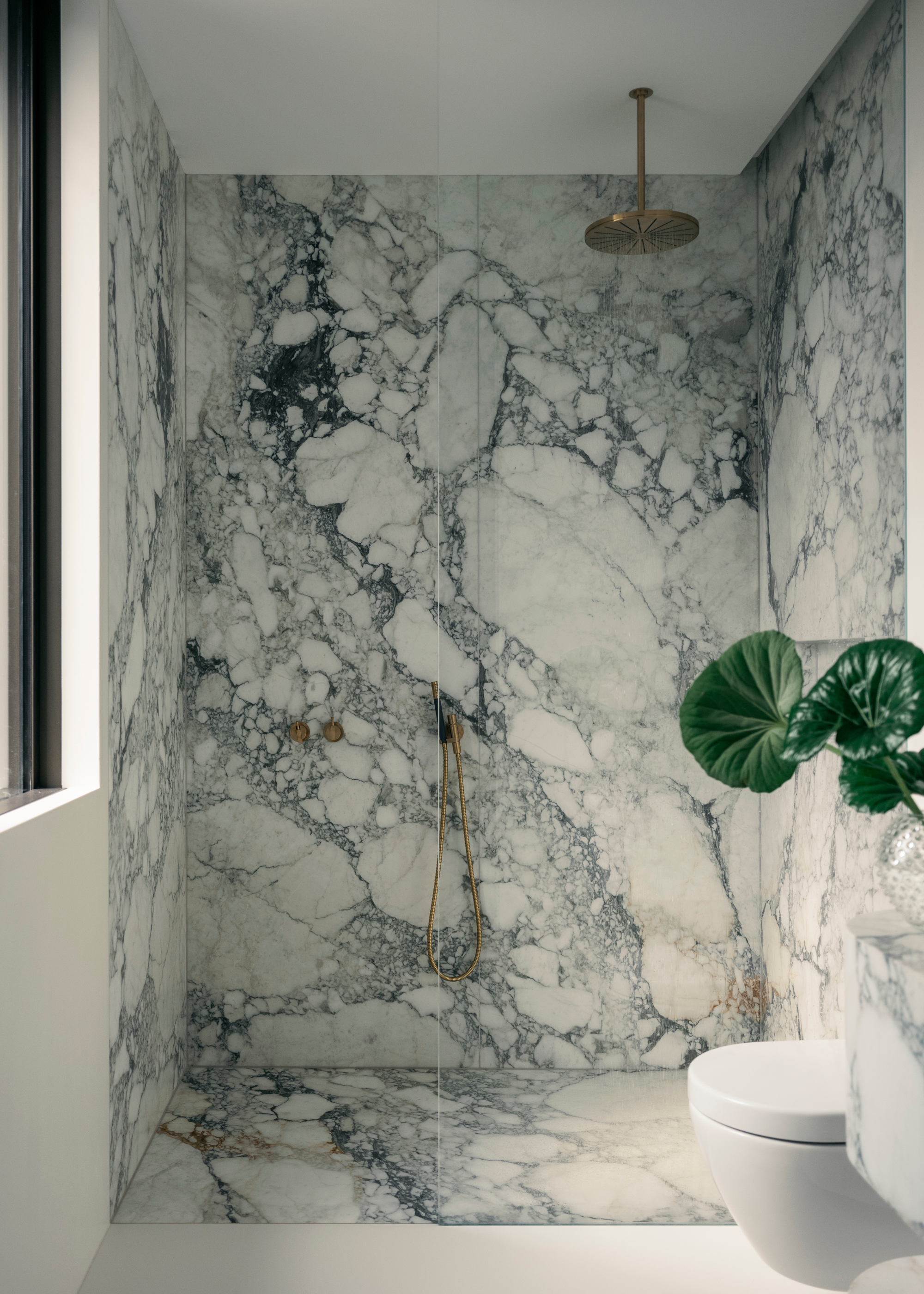 marble clad shower with brass shower head and handheld shower