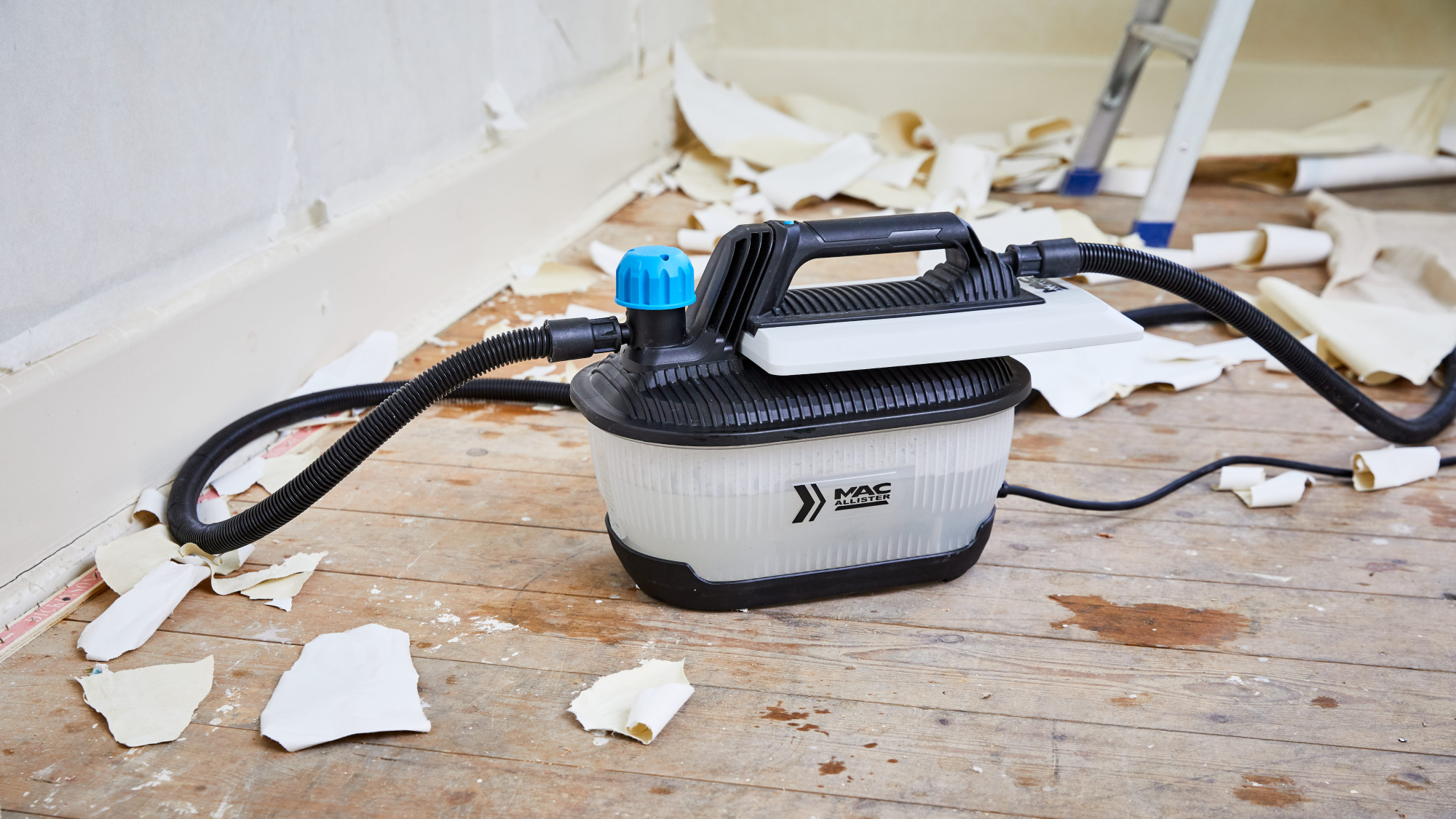 wallpaper steamer on wooden floorboards with wallpaper debris around it
