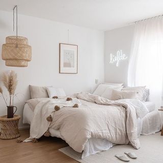 bedroom with bed dressed in linen bedsheets and rattan pendant light and white neon sign