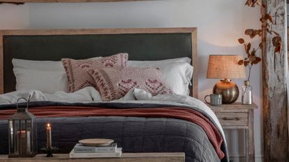 A fall decorated bedroom with a bed with blue padded bedding and green upholstered headboard. Bench at the end of the bed with stacked books and candles