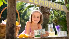 Portrait of girl on lemonade stand holding up one hundred dollar bill