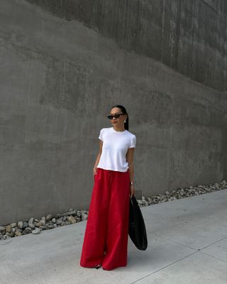 Dawn Tan wearing sunglasses, a white T-shirt, and red wide-leg pants.