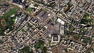 A view looking down from very high at a section of city comprised of buildings and green landscapes.