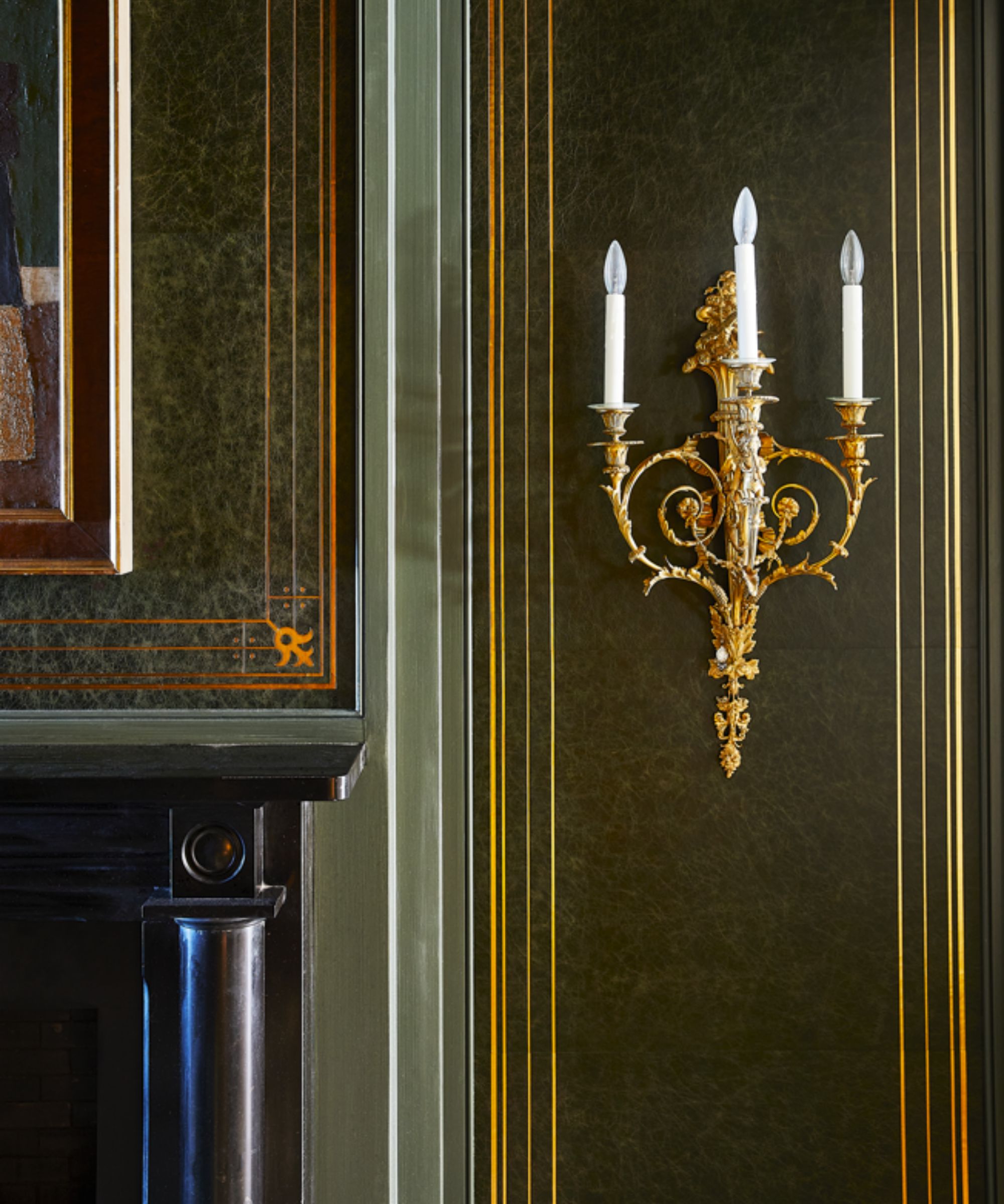 Close up of gold candle sconce on wall, green painted wall with gold trim, black fireplace to the left
