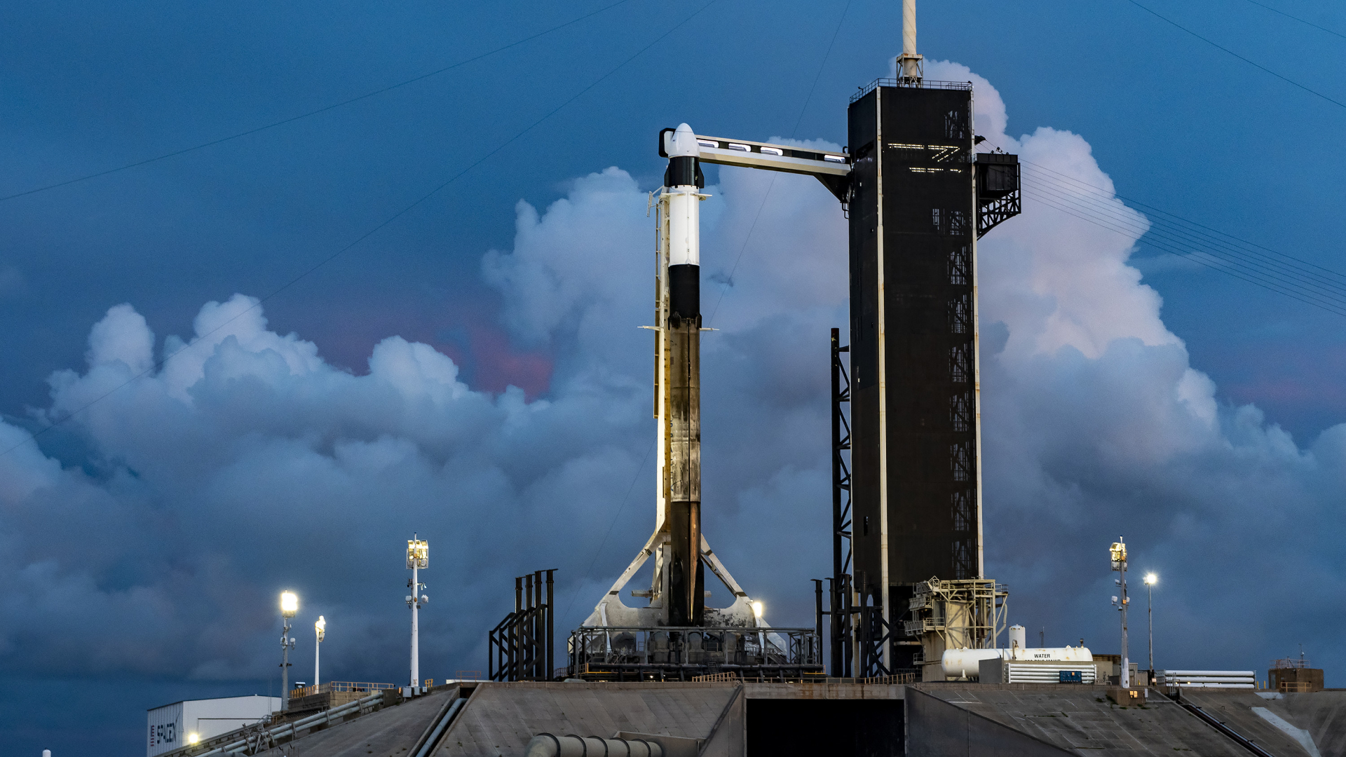 A black and white SpaceX rocket on launch pad with menacing dark clouds in the background