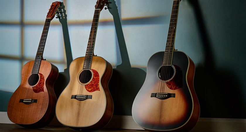 JWJ Guitars&#039; Parlour Select, Orchestra Select and Slope Shoulder Select, all photographed in twilight arranged against a gray-blue wall.