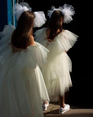 Two girls in identical white flowing dresses standing behind each other with view of their backs.