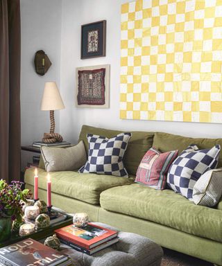 Sitting room with a green sofa and checked cushions, a yellow and white checked wall hanging and candles lit on a table.