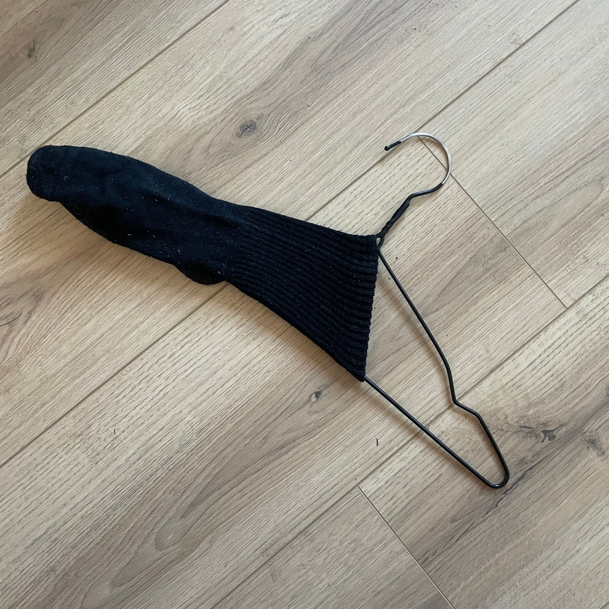 Wire hanger with a black sock over the end of it, on wood-effect flooring