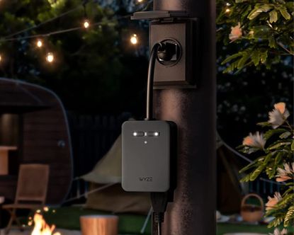 Wyze Outdoor Smart Plug attached to pole in outdoor space beside firepit and seating area