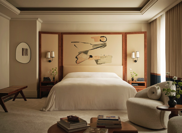 A simple bed draped with a top sheet, with a piece of art on the headboard