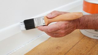 close up of hand painting white paint onto skirting board