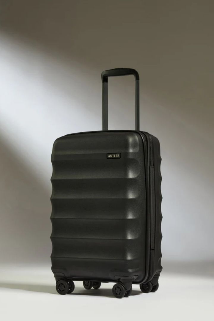 A wavy, glossy black cabin suitecase, photographed against a white background with shadows.