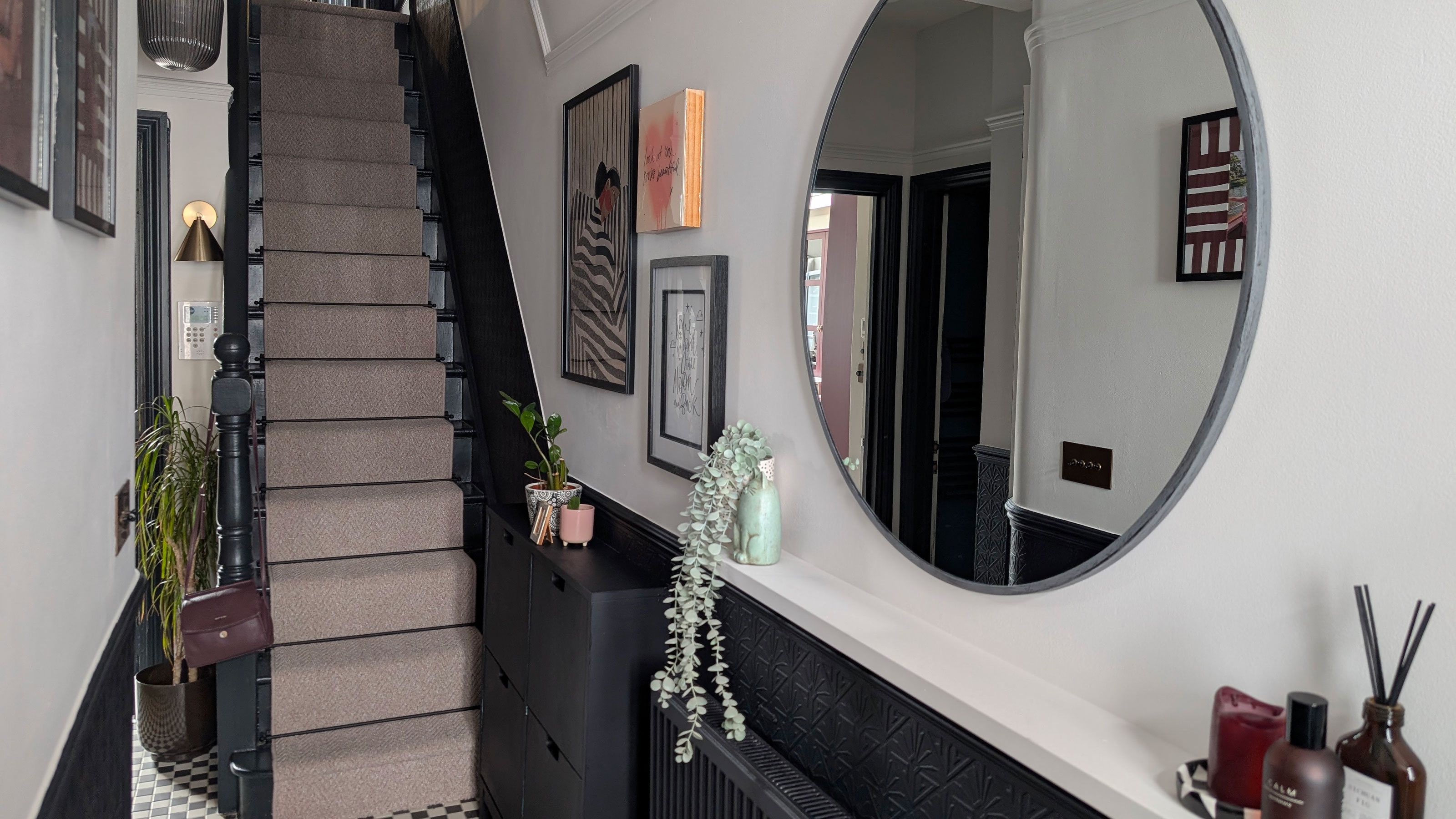 Hallway with lower half of walls painted blue-black, and top half white. Matching blue-black banisters. Large circular mirror on wall