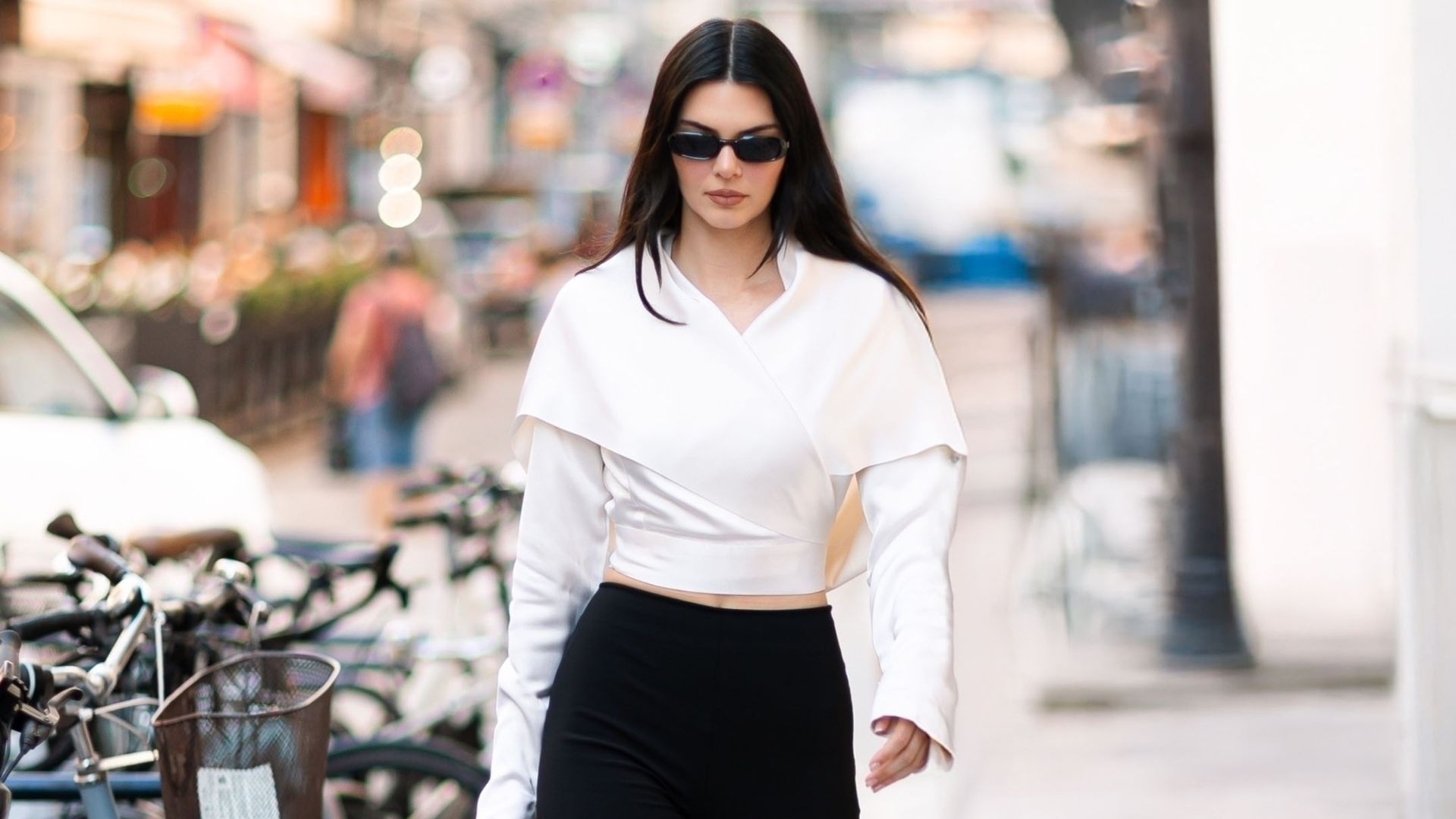 Kendall Jenner walks down the streets of Paris wearing a white wrap top, black high-waisted capri pants and black peep-toe heels. She hold a small black handbag in her clutches as accessories with black sunglasses.