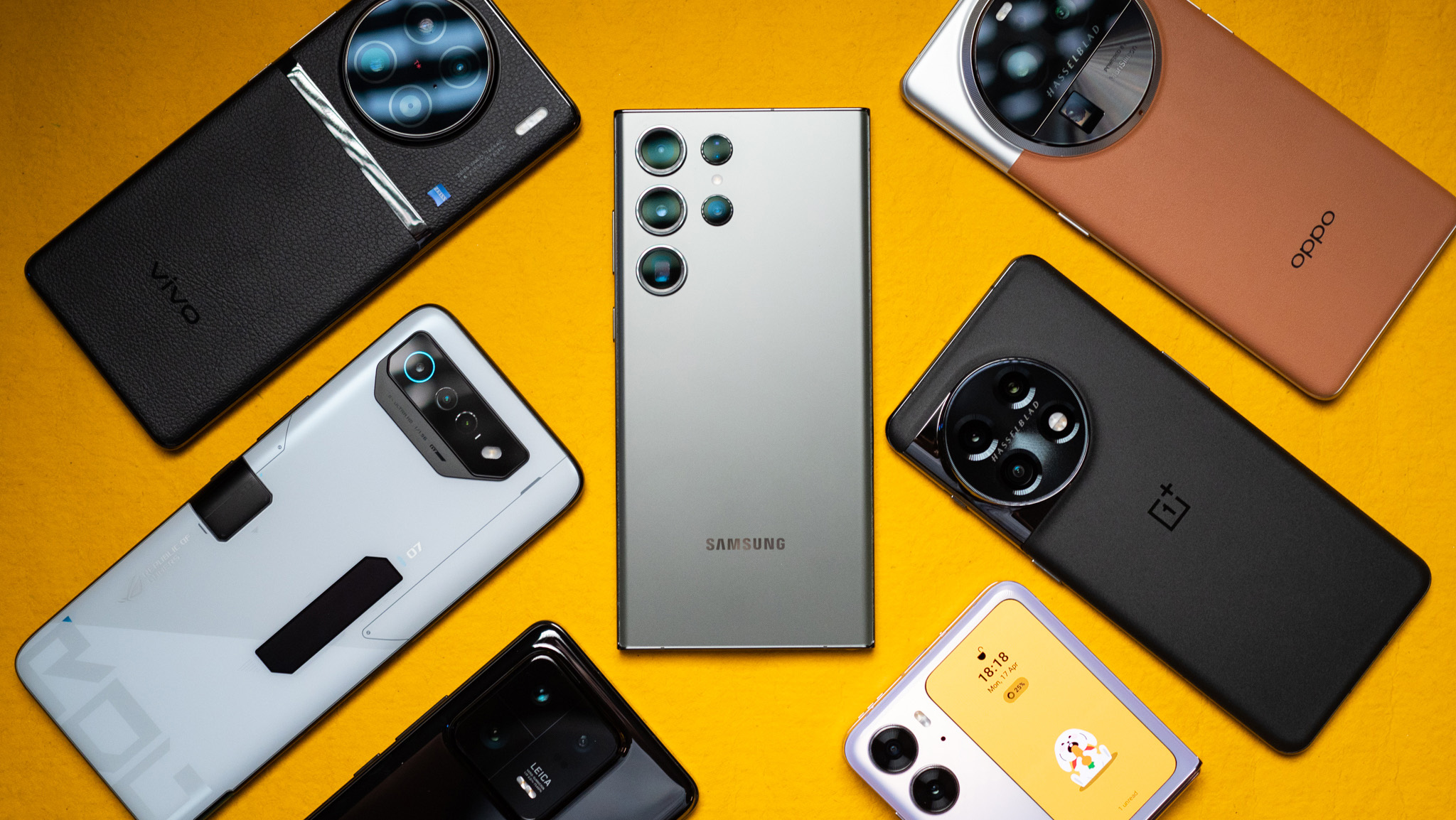 Samsung Galaxy S23 Ultra šalia kitų 2023 Android įrenginių geltoname fone