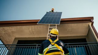 solar panel installer handing solar panel from roof to man on ladder both wearing PPE