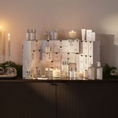 The White Company advent calendar 2025 on a dark wood sideboard next to lit dinner candles
