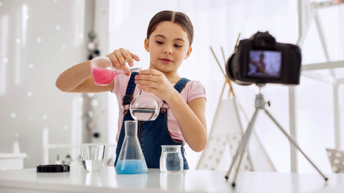 Pre-teen girl recording an interesting chemical experiment and mixing chemicals, pouring a pink one into the water